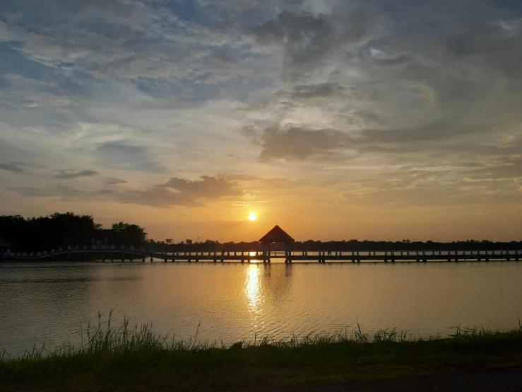 the sun is rising over the water and a long bridge