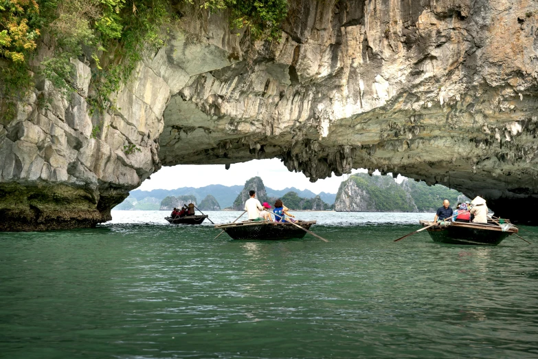 four people paddle their boats past an ancient rock arch