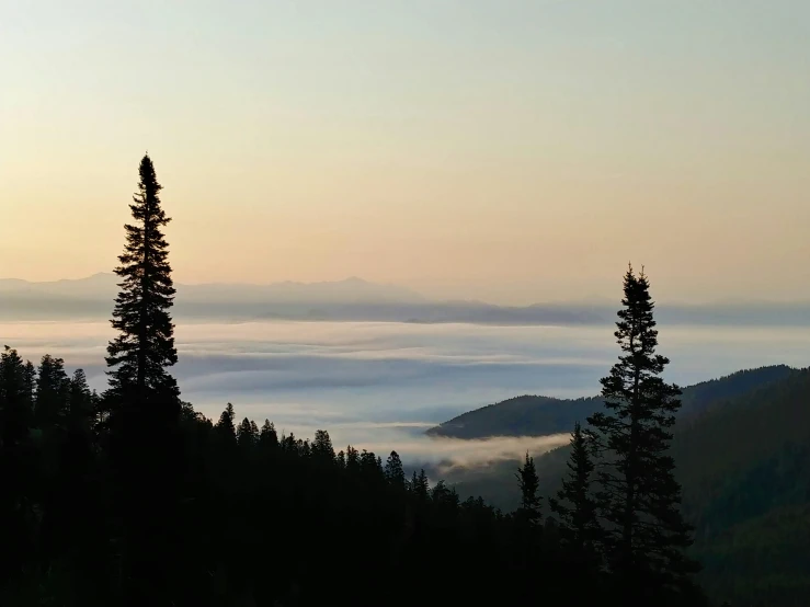 the sky is setting behind some trees and hills