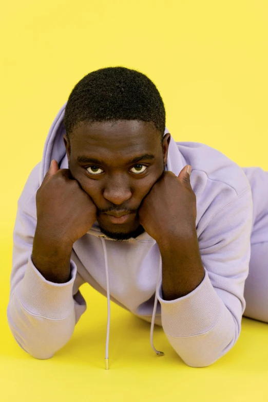 a young man wearing white clothing leaning on his face with a yellow background