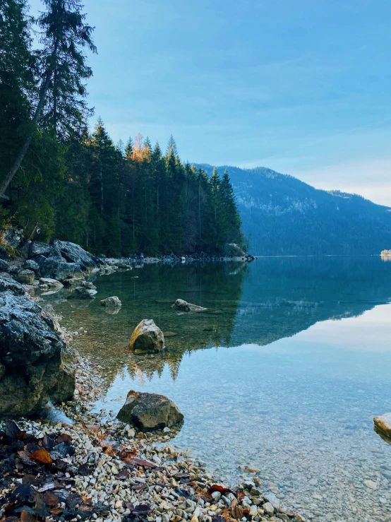 a calm lake with trees, rocks and blue sky