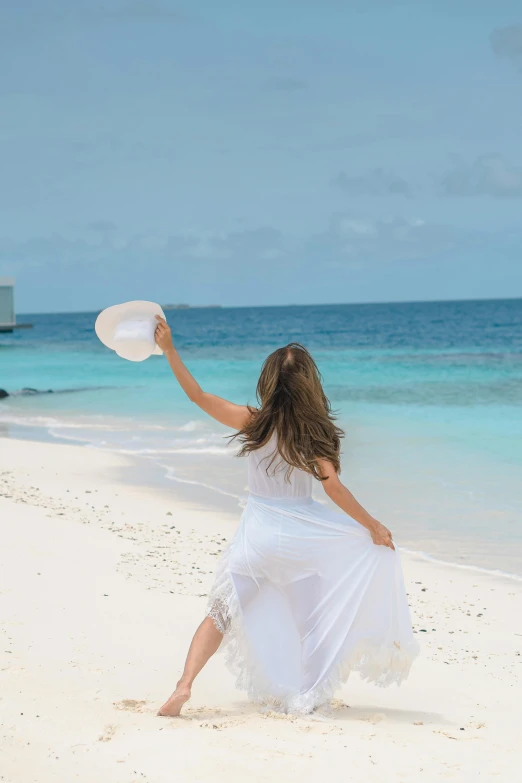 a woman in white dress on the beach throwing a disc