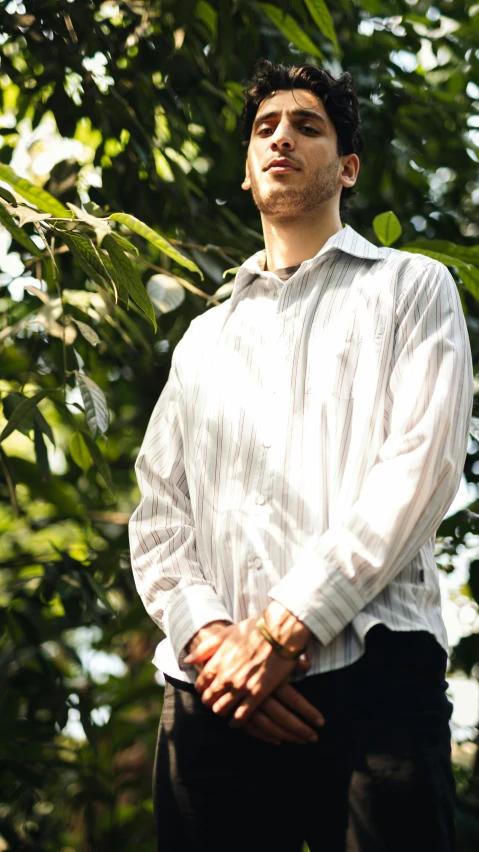 a young man standing in front of a leafy tree