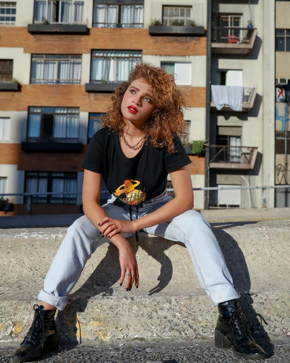 a girl with curly hair sitting down on some ledge