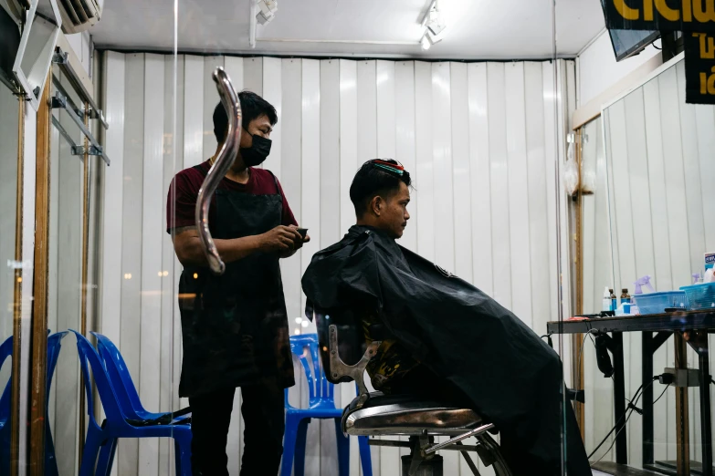 barbers standing next to a man sitting in the chair in a barber shop