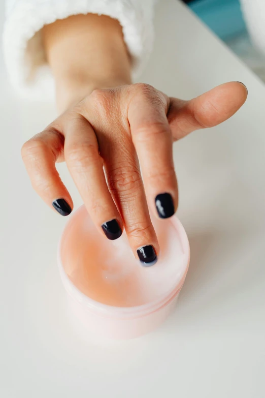 a person with black nail polish holding her hands in front of a container