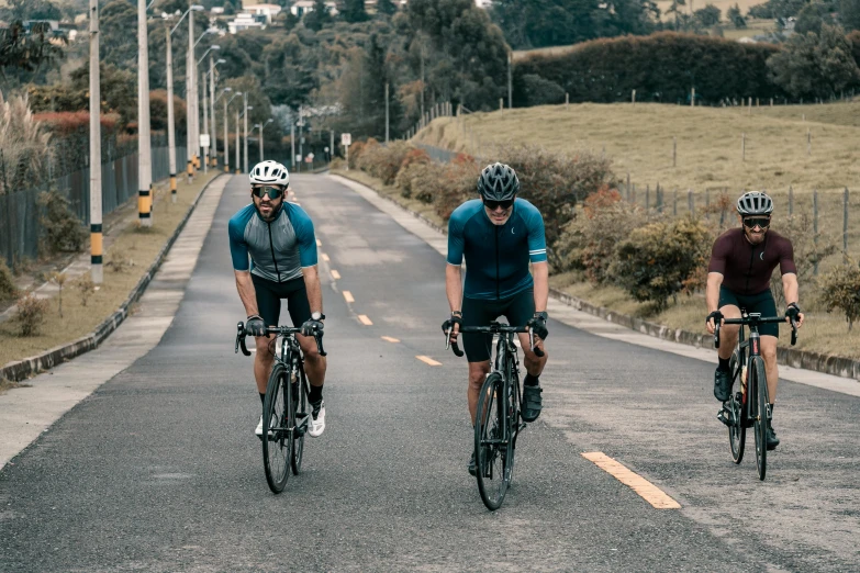 three bicyclists wearing bike helmets, riding down a country road