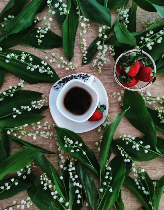 flowers, a cup of coffee and two strawberries are on the table