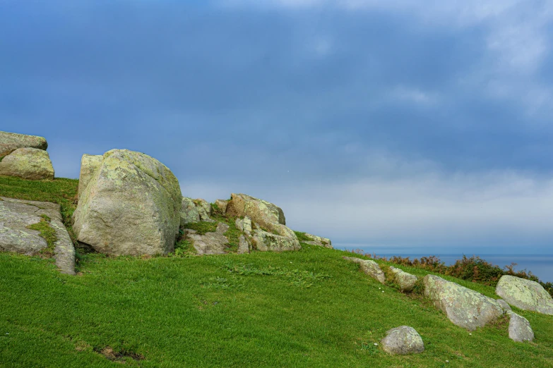 some large rocks in the grass with a body of water behind them