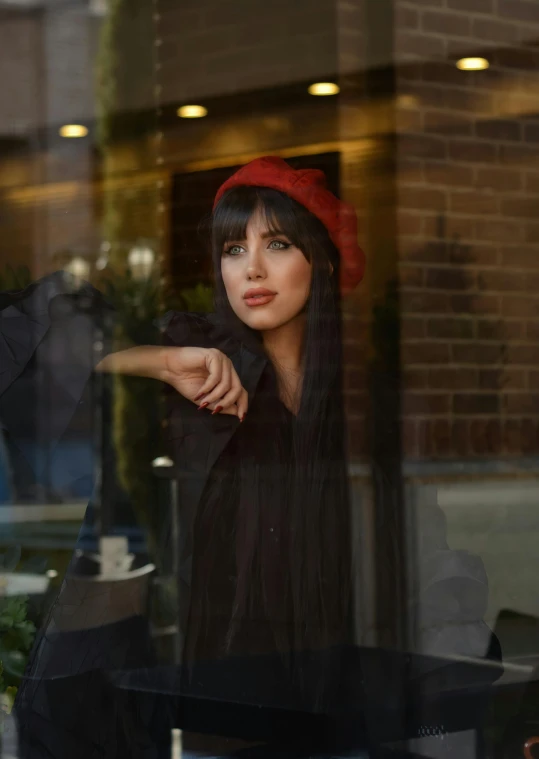 a woman in black dress and red hat next to brick building