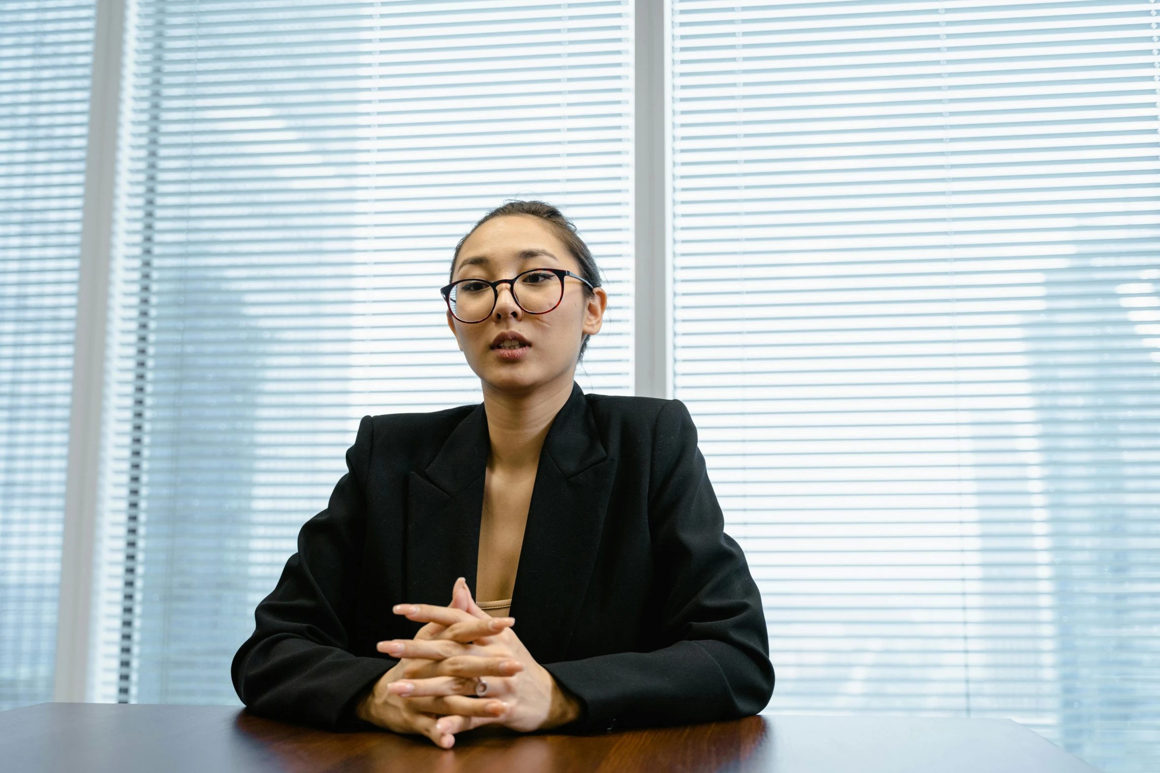 a woman in a business suit is sitting at a wooden desk