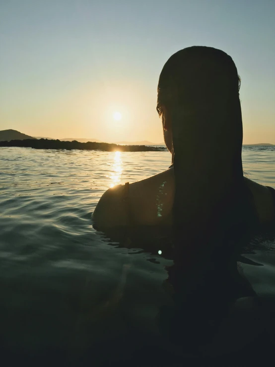 woman swimming alone at sunset in water with head above surface