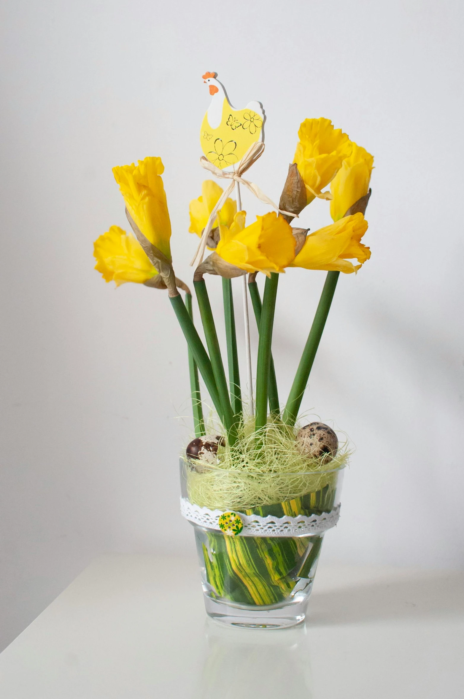 an arrangement of flowers with one little chick on the head in a glass vase