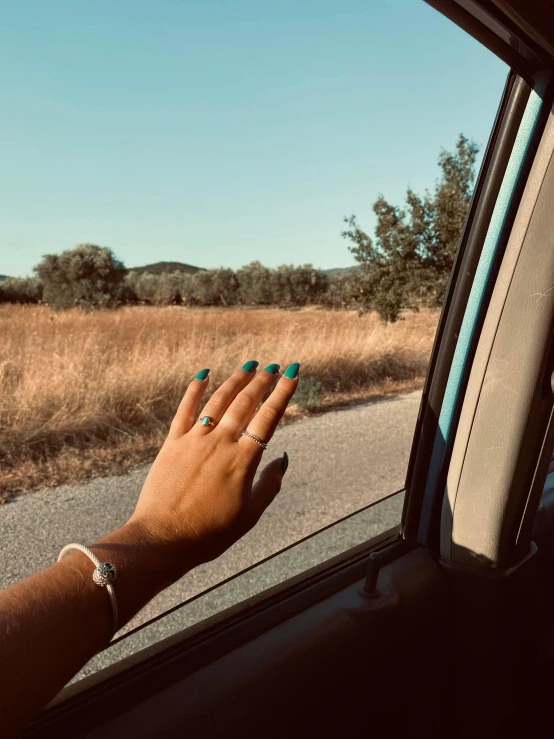 woman's hand out of a car window with a road in the background