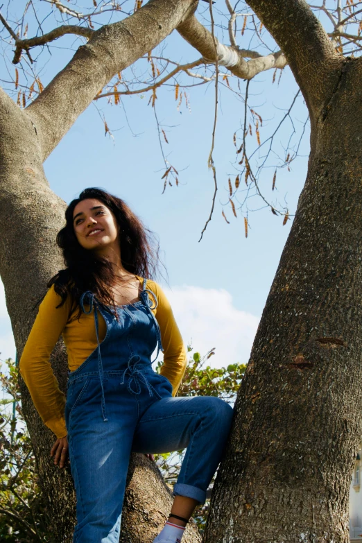 a woman in overalls sitting on a tree in the sun