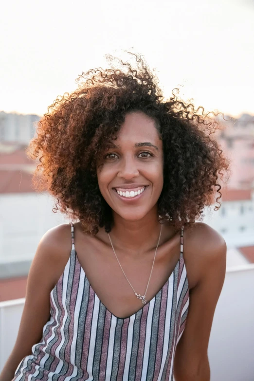 a woman smiling with long curly hair on top of a rooftop