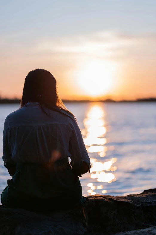 a person sitting on a rock at sunset