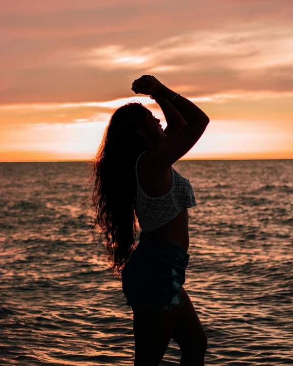 a beautiful young woman standing on top of a beach next to the ocean