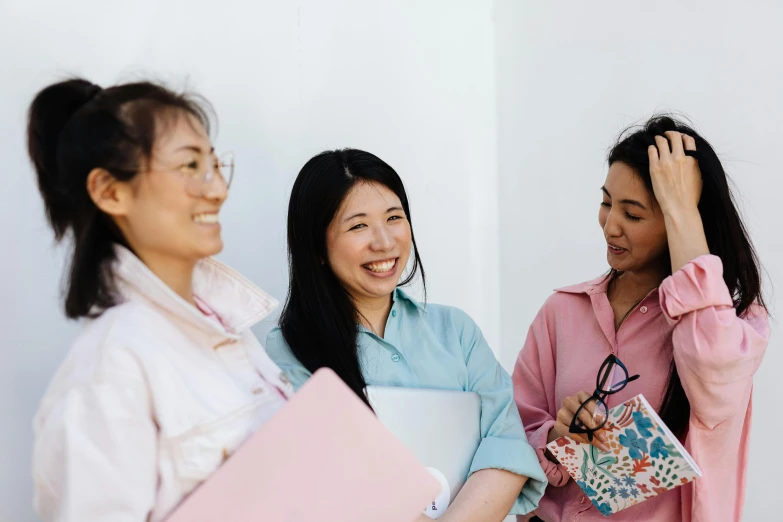 three women laughing with each other while holding folders