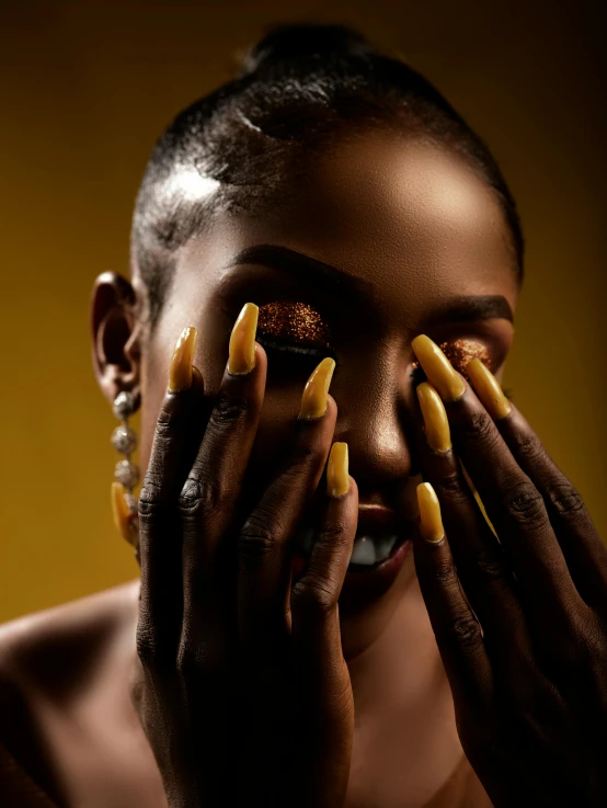 a woman with nail extensions covers her face with yellow manies