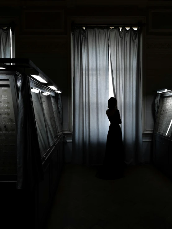 a black and white image of a person standing in the shadows of curtains