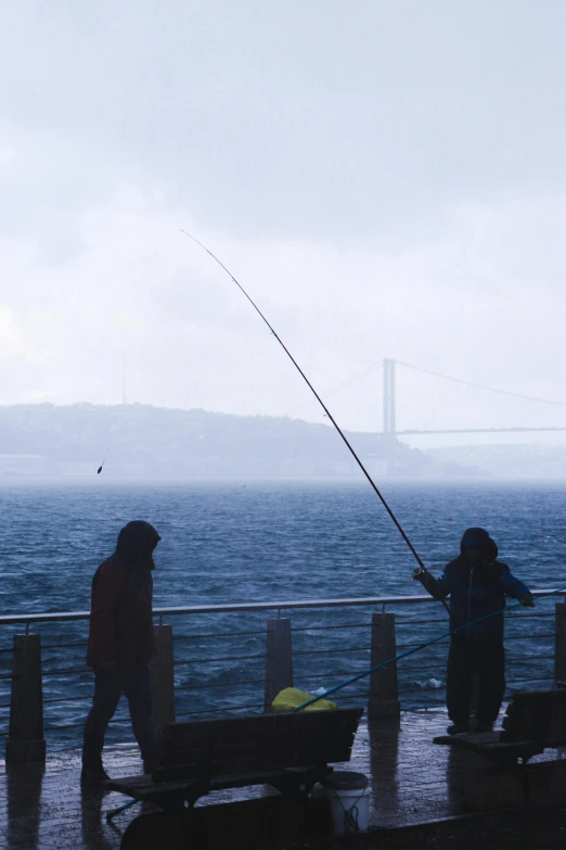 two people are fishing on a pier near the water