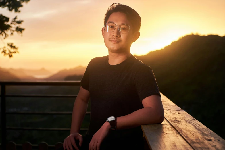 a man with glasses standing at sunset, wearing a black shirt