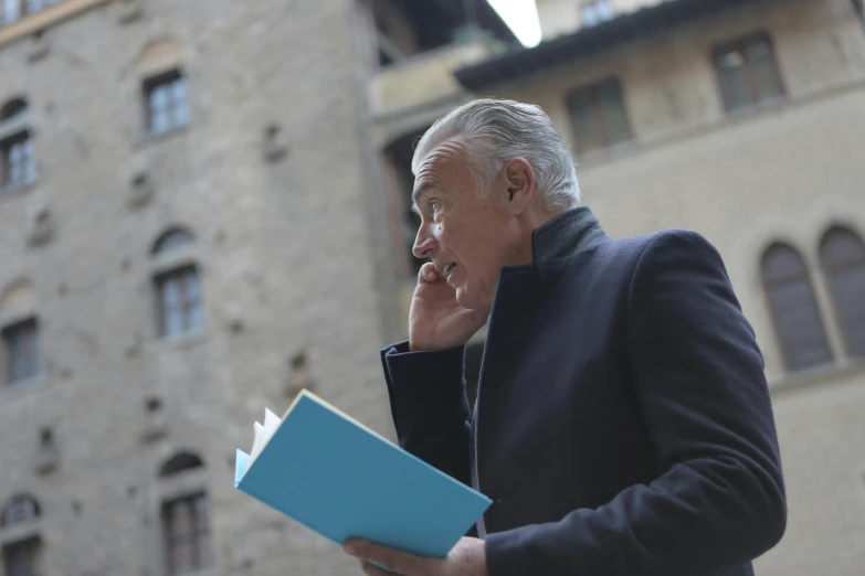 an older man talking on his cell phone while holding a blue folder