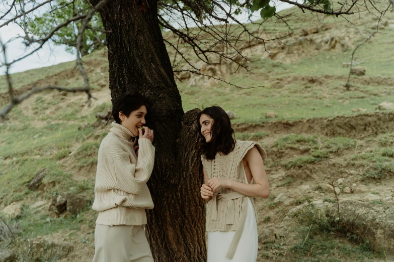 two women standing by a tree in the field