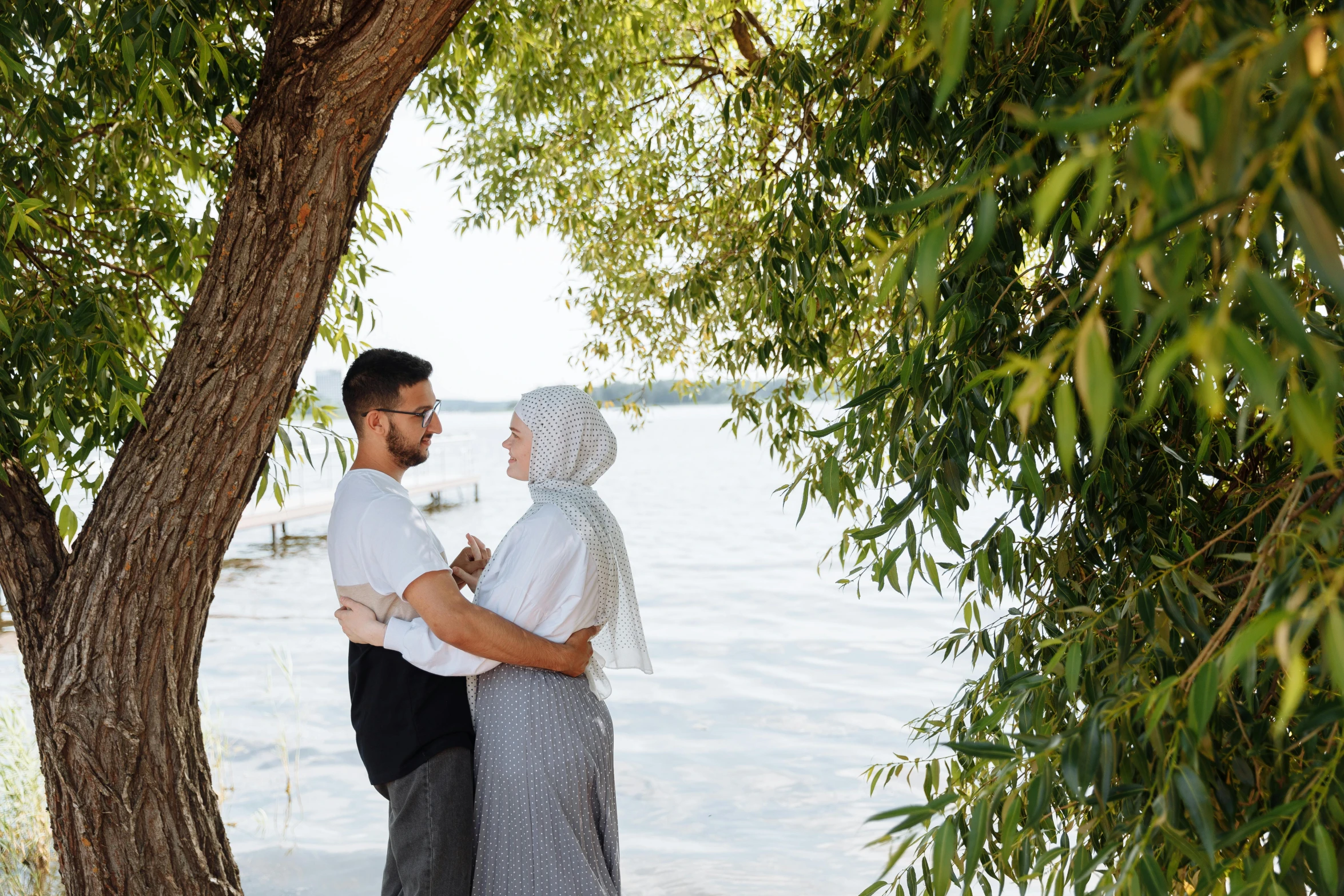 a couple emcing under trees next to a lake