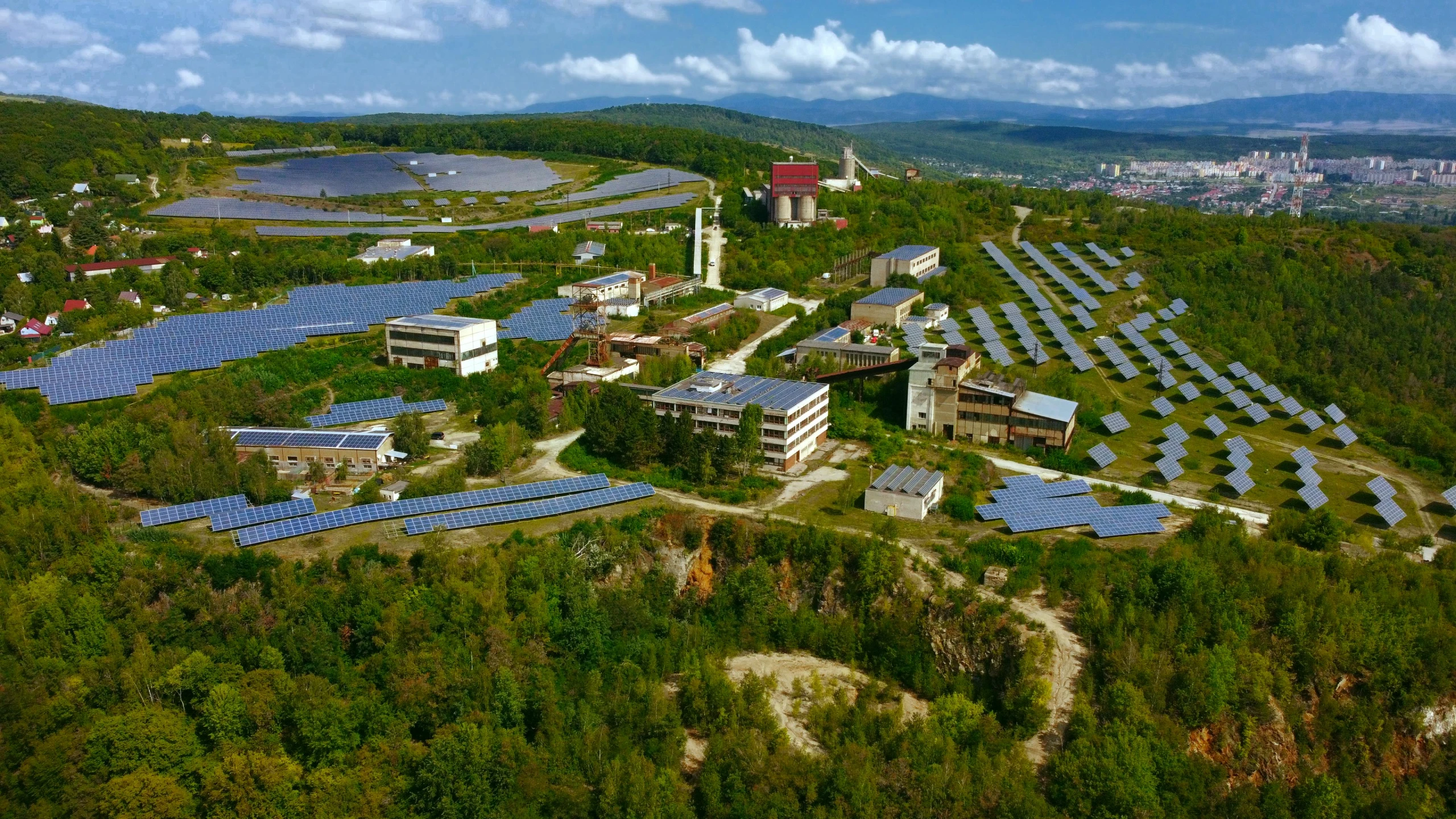 an aerial view of a solar farm with trees, mountains and clouds