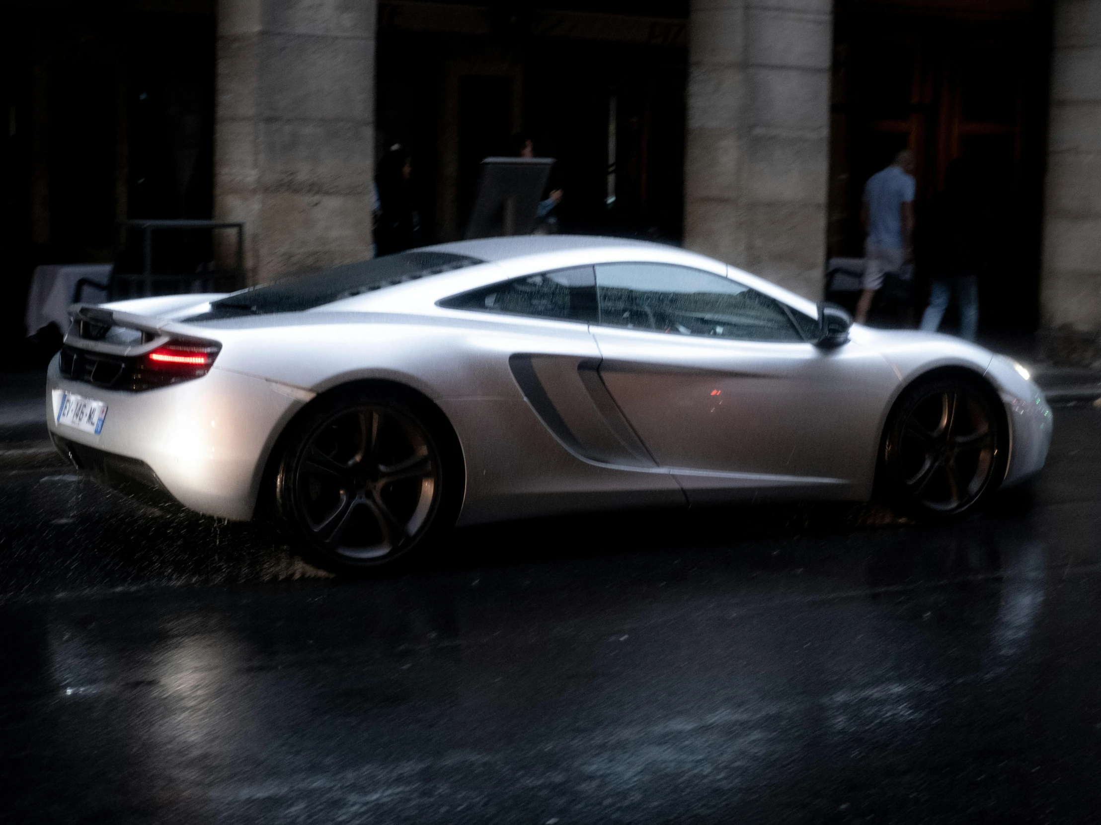 a sports car with its lights on driving down a street in the rain
