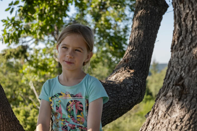 a small child in a tee shirt sitting on the limb of a tree