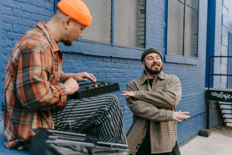 a man leaning against the wall, and another mans standing next to him