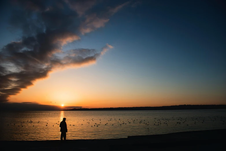 a man stands in the water as the sun sets