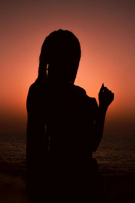 a person stands on the beach at sunset with their hand up to the sky