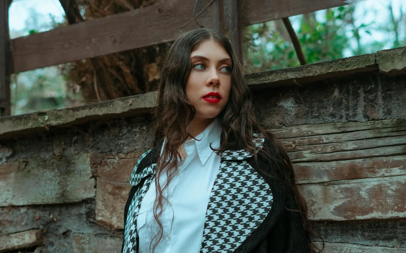 a woman standing near a brick wall and leaning on a wooden fence