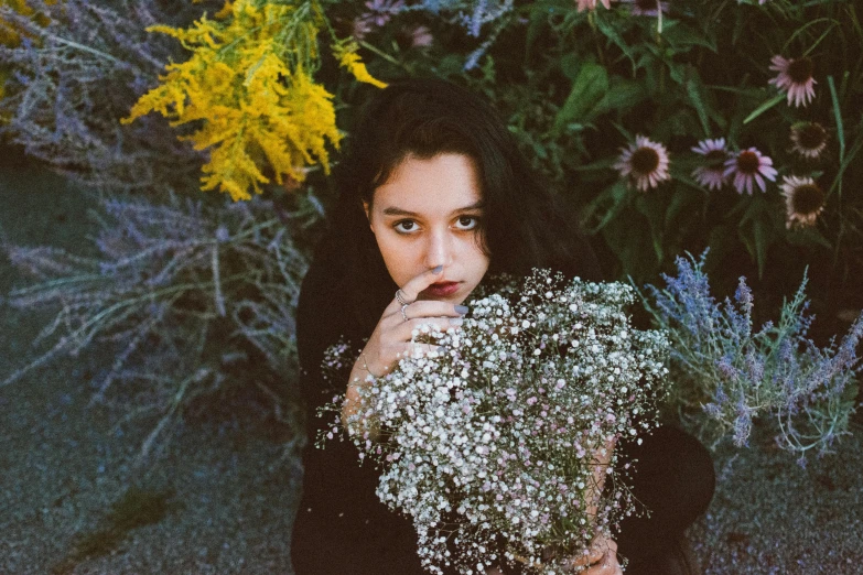 there is a woman holding flowers by the bushes