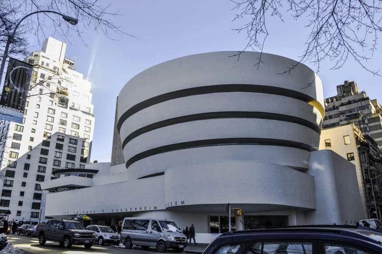 the building is shaped like a shell, but has a circular entrance that leads up to a parking lot with lots of cars parked inside of windows