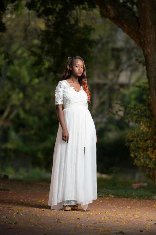 woman in white dress standing against tree trunk