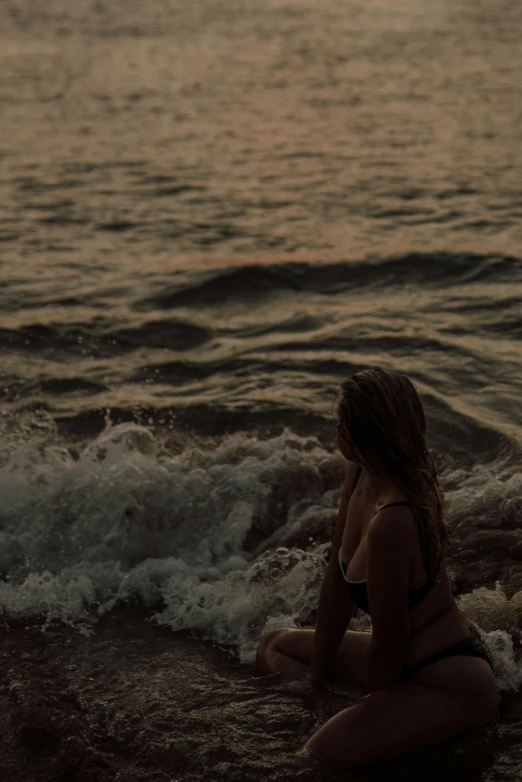 a woman in black swimsuit sitting on sand by the ocean