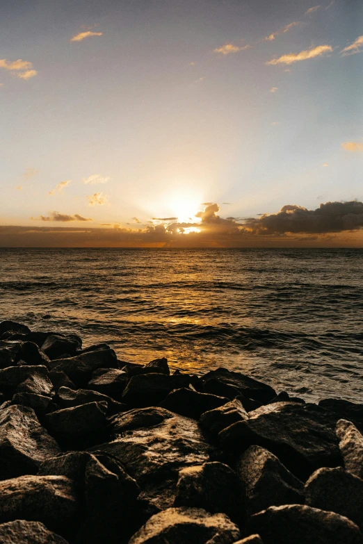 the sun setting on the sea and rocks by the shore