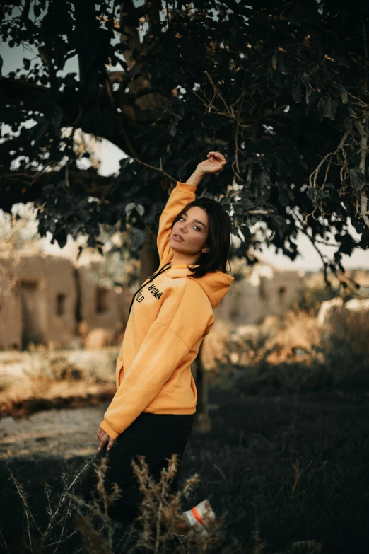 a woman stands in a field next to a tree