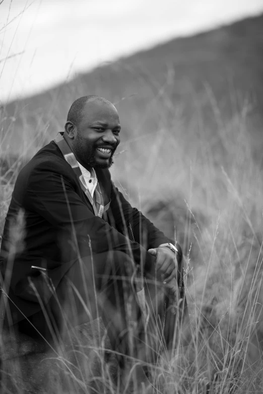 a black man sits on a grassy hill and smiles