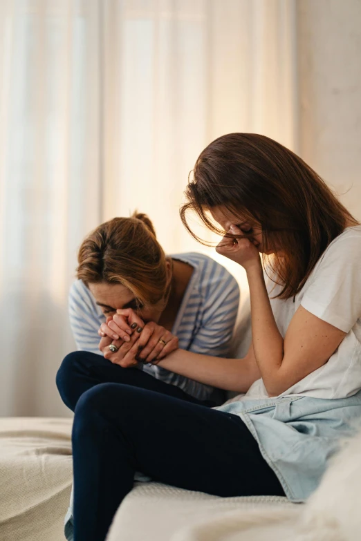 a woman is sitting on a bed as another woman covers her face