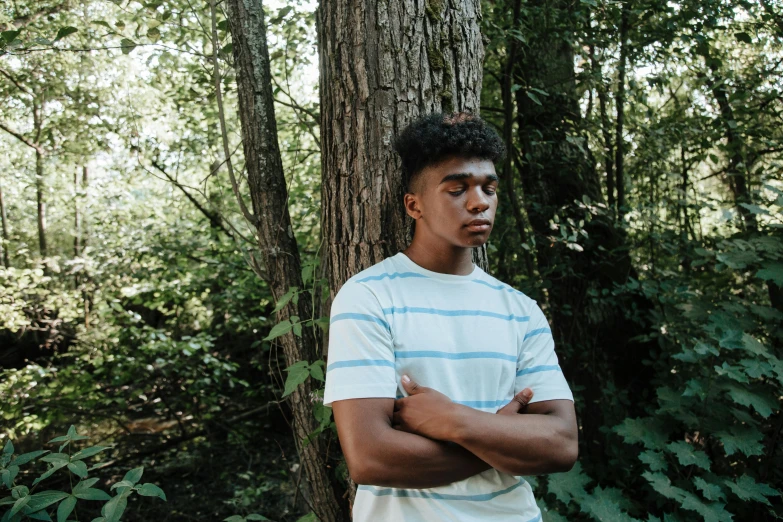 a young man standing in front of a tree in the forest