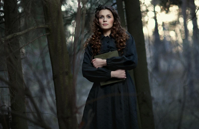 a woman standing outside in the woods while wearing a black dress