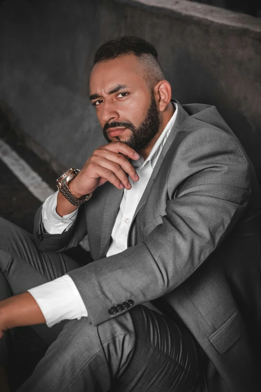 a man wearing a suit and a watch sits on concrete