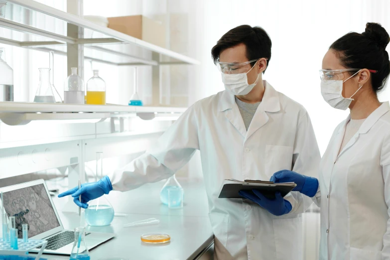 two people wearing masks and gloves and holding beaks, working in a lab