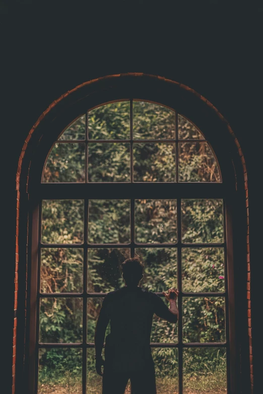 a young man standing in an arched window with the sun shining through